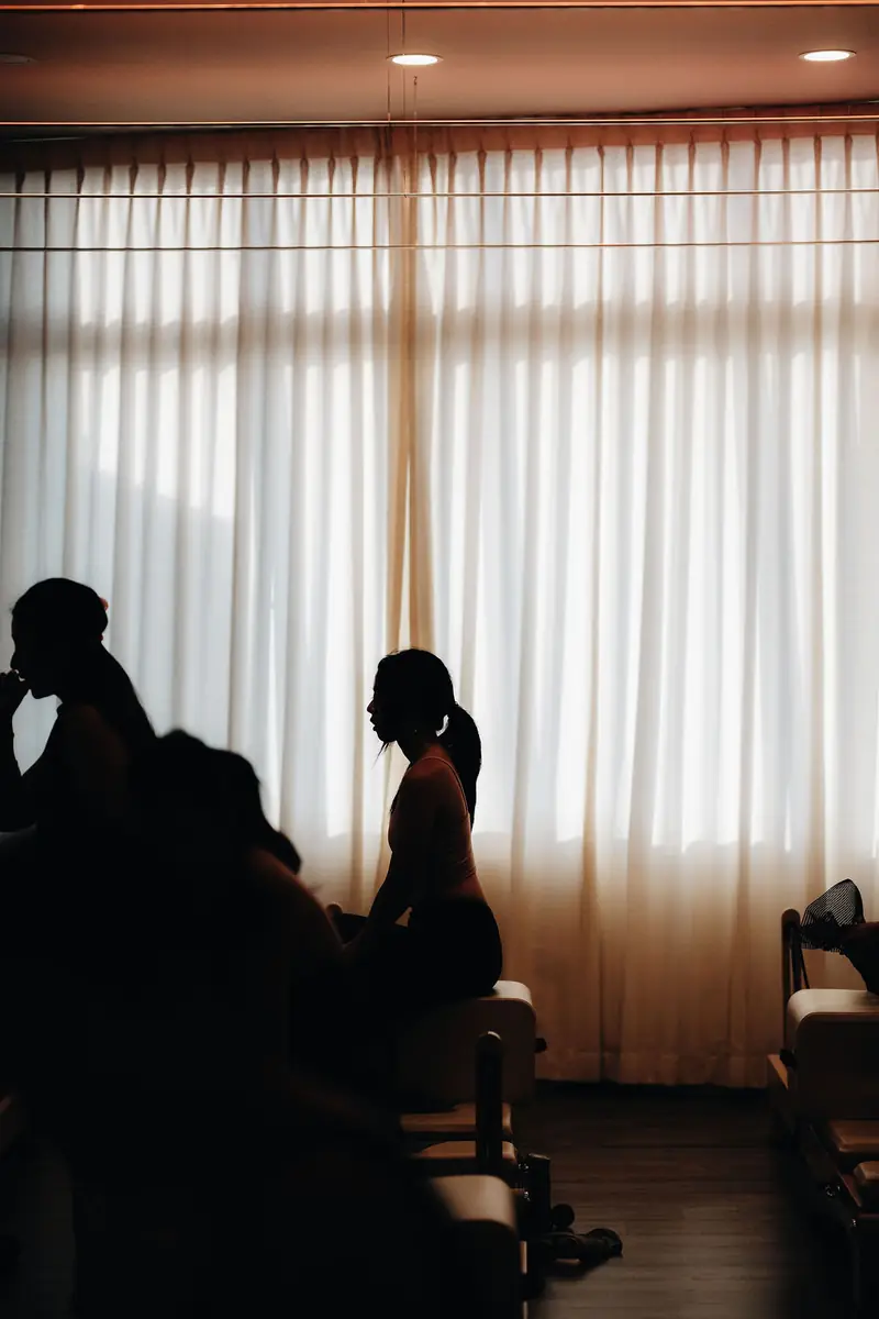 Silhouettes of clients on reformers against white curtains